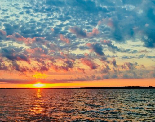 A vibrant sunset over a calm body of water, with colorful clouds reflecting the warm hues of the sky.