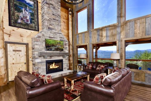 Cozy living room with a stone fireplace, large windows, and mountain views, featuring leather sofas and rustic decor.