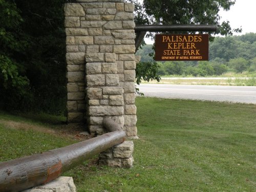 Sign for Palisades Kepler State Park, featuring stone structure and wooden beam, set against a green landscape.