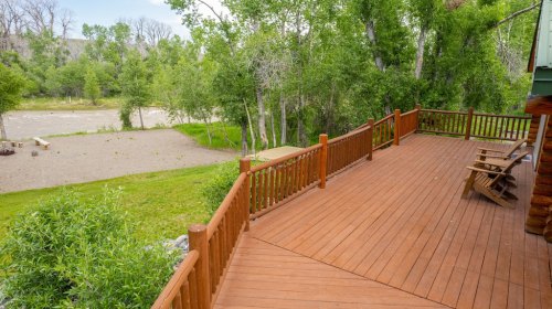 A wooden deck overlooking a grassy area and a river, surrounded by lush green trees.