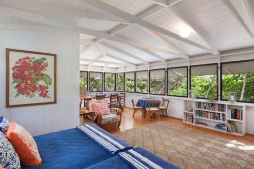 Bright, airy living space with large windows, a blue sofa, floral artwork, and cozy seating areas surrounded by greenery.