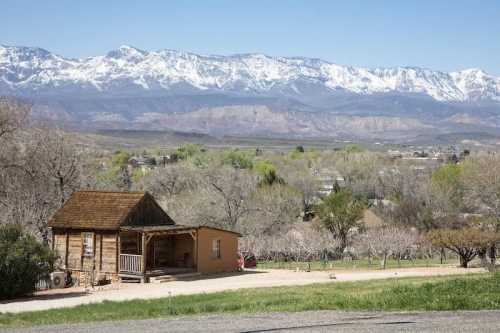 A rustic cabin in the foreground with snow-capped mountains and a clear blue sky in the background.