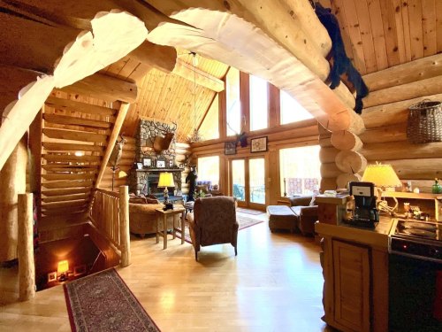 Cozy log cabin interior featuring a staircase, large windows, and rustic furnishings. Warm and inviting atmosphere.
