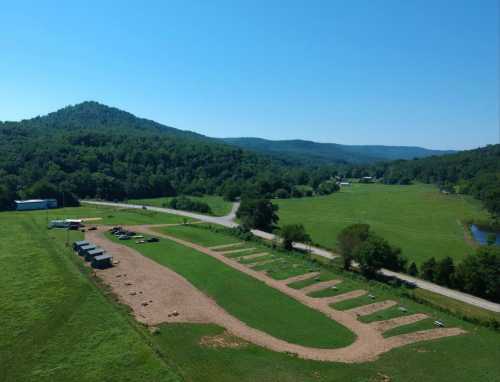 Aerial view of a green landscape with a road, mountains in the background, and a cleared area with marked spaces.