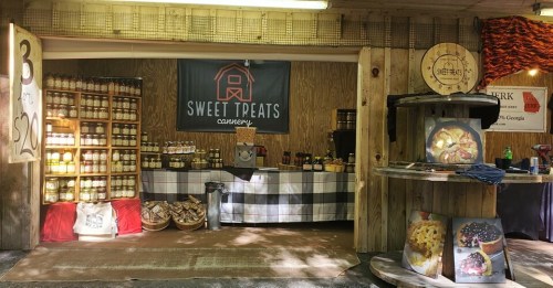 A cozy market stall featuring jars of preserves, a checkered tablecloth, and a sign for "Sweet Treats Cannery."