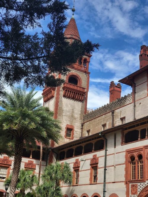 A historic building with red and white architecture, featuring a tall clock tower and surrounded by palm trees.