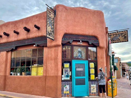 A colorful adobe building with a turquoise door and decorative signs, set against a cloudy sky.