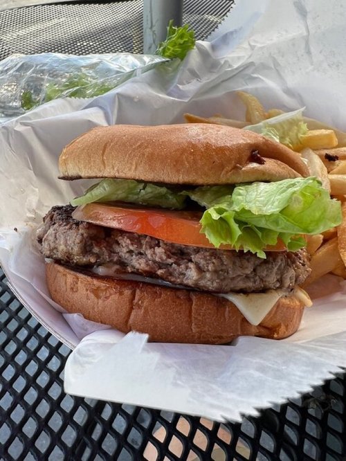 A juicy hamburger with lettuce, tomato, and cheese, served with a side of fries in a takeout container.