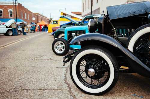 A row of classic cars with whitewall tires parked on a street during a car show.