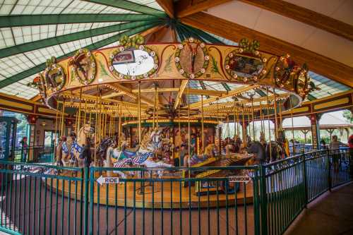 A colorful carousel with ornate horses, surrounded by a fence, under a bright, glass-roofed pavilion.