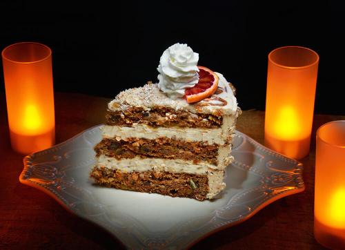 A slice of layered cake topped with whipped cream and orange slice, surrounded by glowing orange candles.