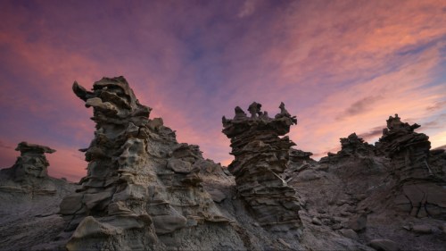 Rock formations rise against a colorful sunset sky, showcasing unique shapes and textures in a desert landscape.