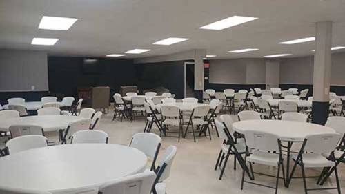 A spacious room with multiple round tables and chairs, well-lit with overhead lights and a neutral color scheme.