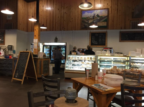 A cozy café interior with wooden walls, a display case of pastries, and customers at the counter.