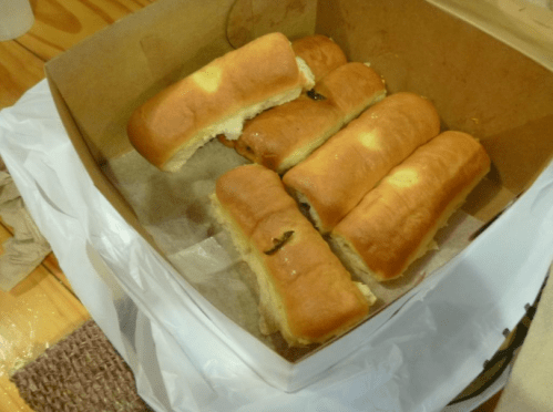 A box containing several soft, golden-brown hot dog buns, some partially cut open.
