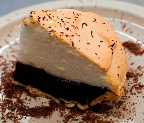 A slice of chocolate meringue pie topped with fluffy meringue and chocolate shavings on a plate.