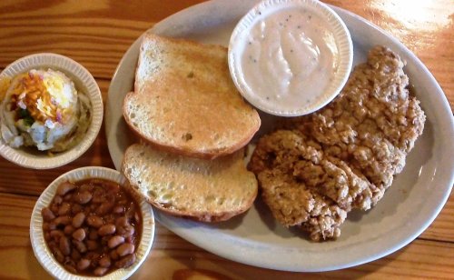 A plate with fried chicken strips, toast, baked beans, and a side of creamy sauce.