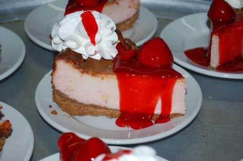 A slice of cheesecake topped with whipped cream and strawberry sauce, served on a white plate.