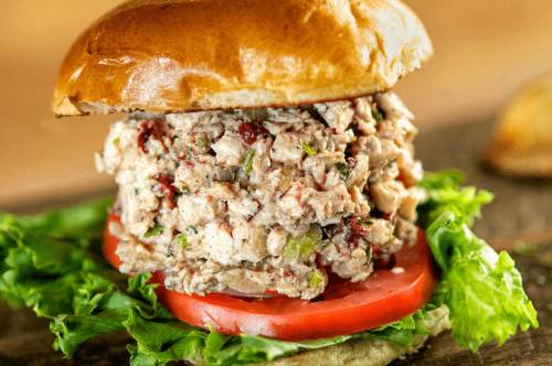 A close-up of a sandwich featuring a thick layer of chicken salad, lettuce, and tomato on a toasted bun.