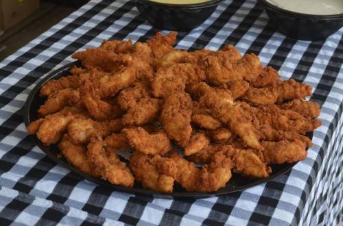 A large platter of golden-brown fried chicken tenders on a black and white checkered tablecloth.