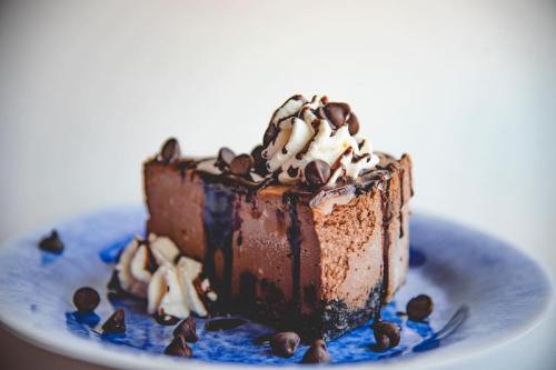 A slice of chocolate cake topped with whipped cream and chocolate chips, served on a blue plate.