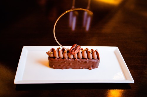 A chocolate dessert on a white plate, topped with chocolate mousse, a pecan, and a decorative sugar swirl.