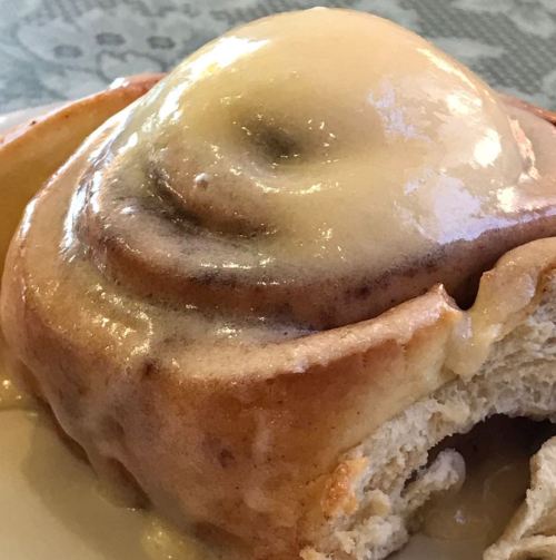 A close-up of a cinnamon roll topped with creamy icing, showcasing its swirled layers and soft texture.