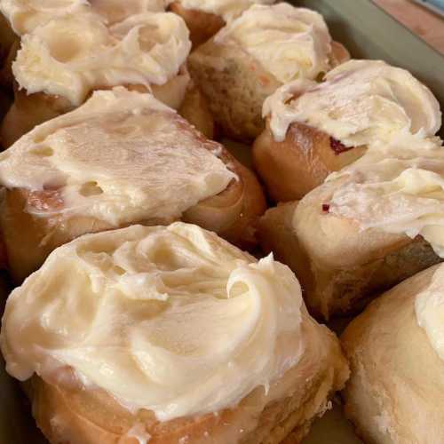 A close-up of freshly baked cinnamon rolls topped with creamy frosting on a green plate.