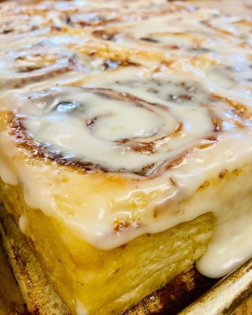 Close-up of freshly baked cinnamon rolls drizzled with creamy icing, showcasing their soft, gooey texture.