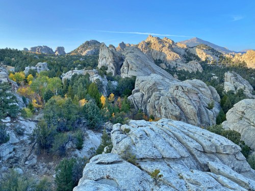 A scenic view of rugged rock formations surrounded by trees and mountains under a clear blue sky.