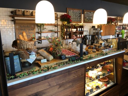 A cozy bakery counter filled with various breads, pastries, and holiday decorations, with staff preparing orders.
