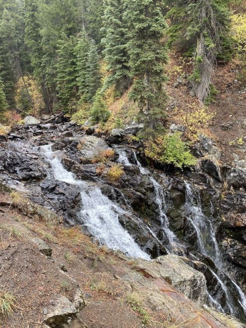 A serene waterfall cascading over rocky terrain, surrounded by lush green trees and autumn foliage.