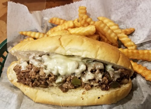 A sandwich filled with ground beef and melted cheese, served with crinkle-cut fries on the side.
