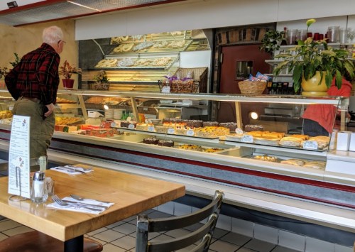 A man in a plaid shirt looks at a display case filled with various pastries in a cozy café.