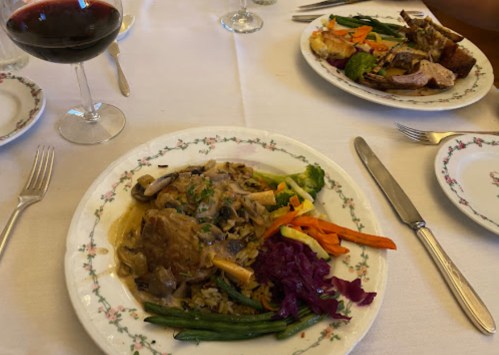 A plate of chicken with mushrooms and rice, served with colorful vegetables and a glass of red wine.