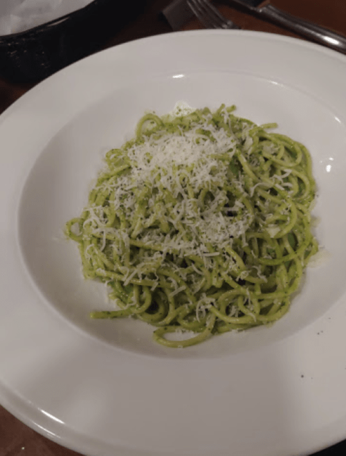 A plate of spaghetti tossed in green pesto, topped with grated cheese.
