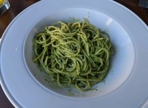 A bowl of spaghetti tossed in green pesto sauce, garnished with grated cheese.