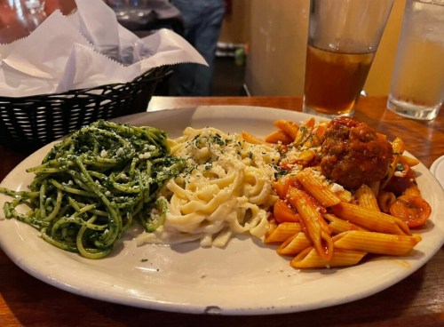 A plate with three types of pasta: green pesto, fettuccine alfredo, and penne with meatballs and marinara sauce.