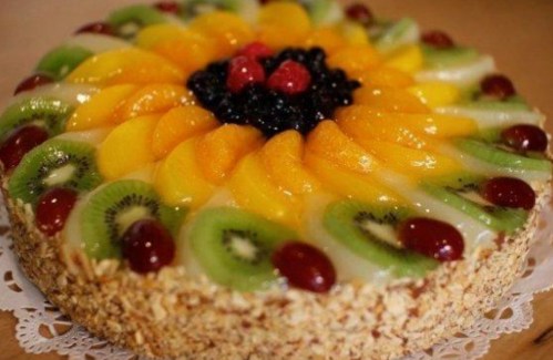 A colorful fruit cake topped with kiwi, peaches, grapes, and berries arranged in a floral pattern.