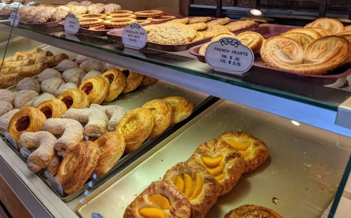A display of assorted pastries, including chocolate cookies, fruit tarts, and flaky croissants, in a bakery.