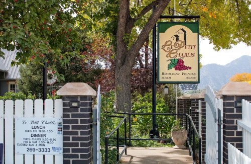 Sign for Le Petit Chablis restaurant, featuring a French theme, with trees and mountains in the background.