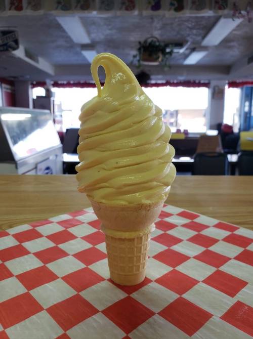 A tall swirl of soft-serve ice cream in a cone, set on a red and white checkered tablecloth.
