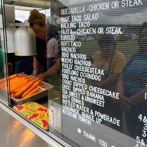 A food truck menu featuring various items like tacos, burritos, nachos, and desserts, with a person preparing food.