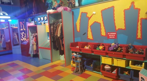 Colorful playroom with costumes hanging, toy bins, and vibrant wall art featuring city skyline silhouettes.