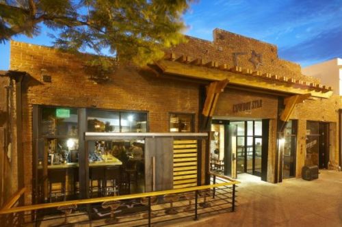Exterior view of a rustic brick restaurant with wooden accents and large windows, set against a twilight sky.