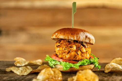 A delicious burger with a crispy patty, lettuce, tomato, and a toasted bun, served with potato chips on the side.
