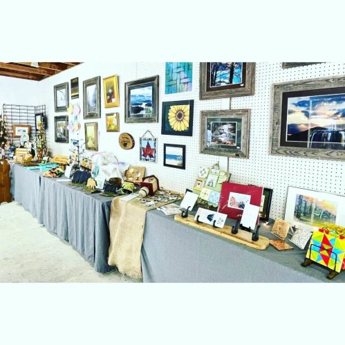 A display of various artworks and crafts on tables, featuring framed pictures, sculptures, and decorative items.