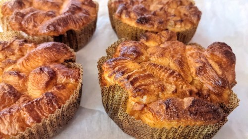 Four golden-brown pastries in textured paper cups, with a crispy, flaky top and a soft interior.