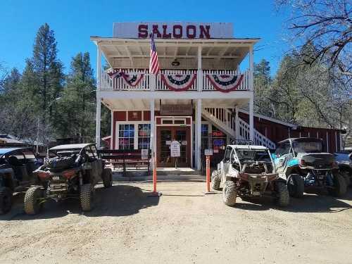 A rustic saloon building with an American flag, surrounded by off-road vehicles in a forested area.