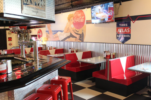 Retro diner interior with red booths, a black and white checkered floor, and vintage Coca-Cola decor.